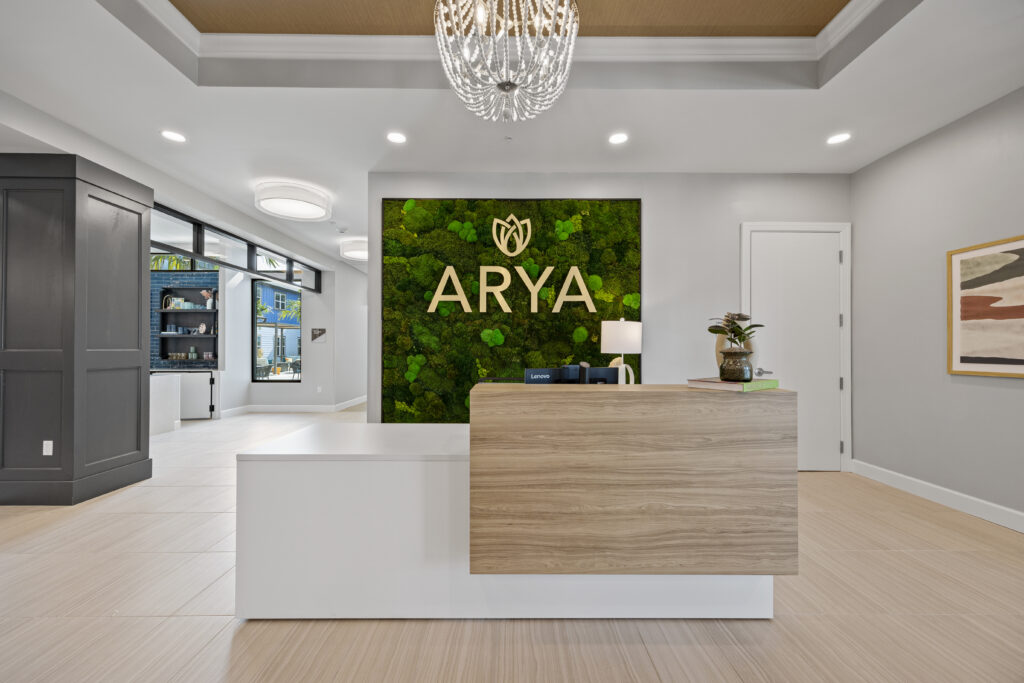 Reception desk with wood accents and green moss ARYA logo wall at Arya at DeBary.