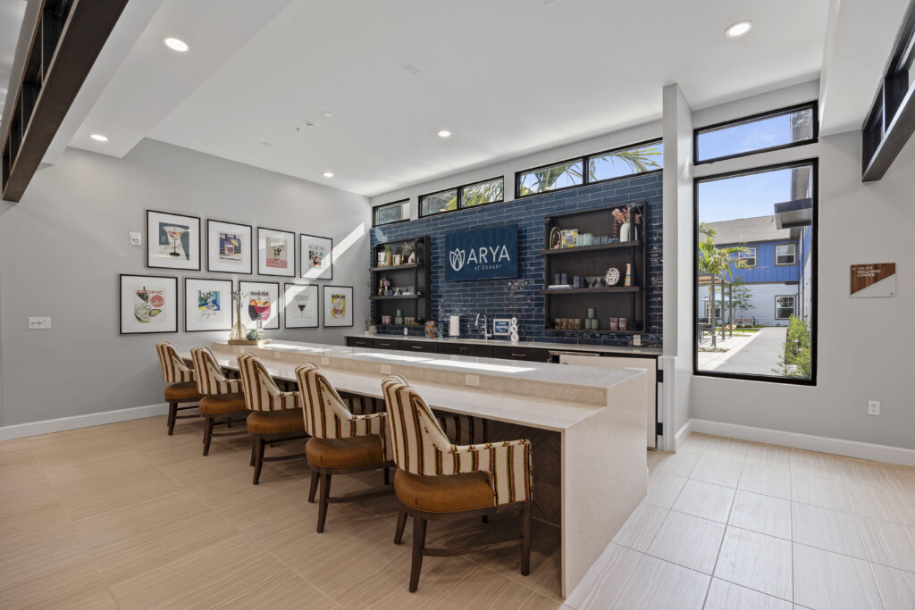 Bar and lounge with striped chairs, art, and open shelving at Arya at DeBary.