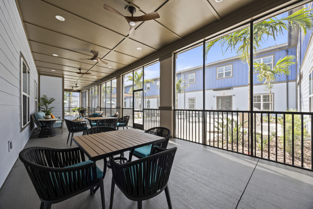 Screened patio area offering comfortable seating, tables, ceiling fans, and views of the lush outdoor courtyard.