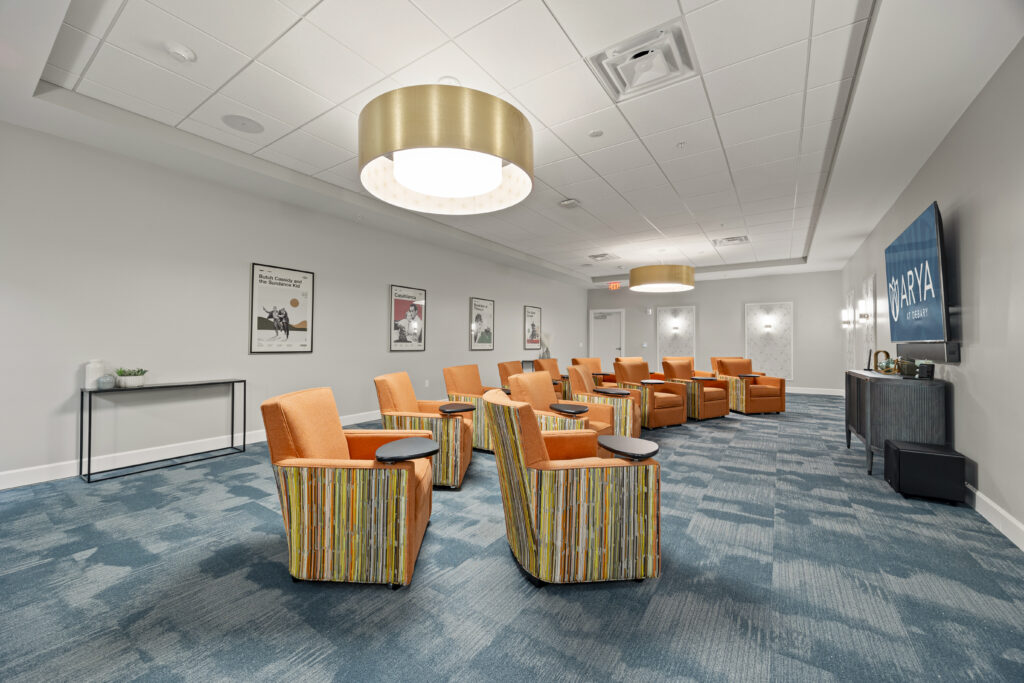 Theater room with comfortable orange chairs, movie posters, large TV screen, and ARYA branding.
