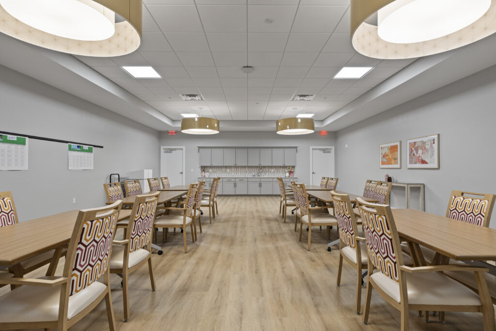 Bright activity space showing symmetrical tables, artistic chairs, pendant lights, and framed artwork.