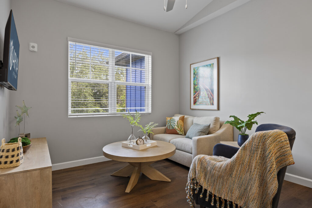 Cozy living room with sofa, armchair, wooden coffee table, large window, and vibrant wall art.