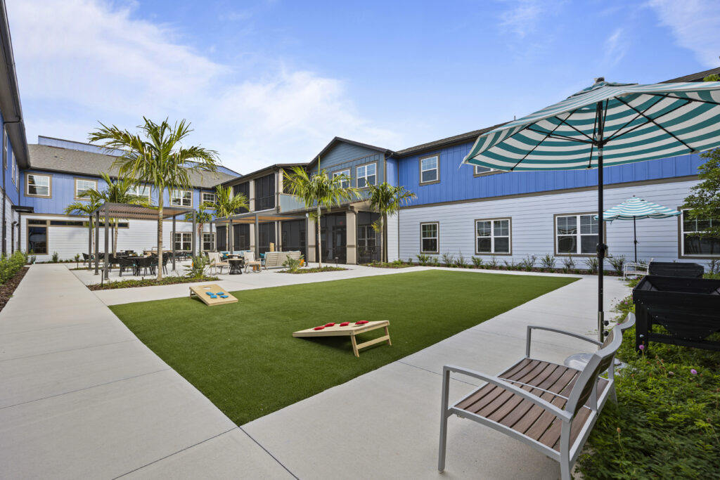Courtyard with turf lawn, palm trees, seating areas, and cornhole game at Arya at DeBary.