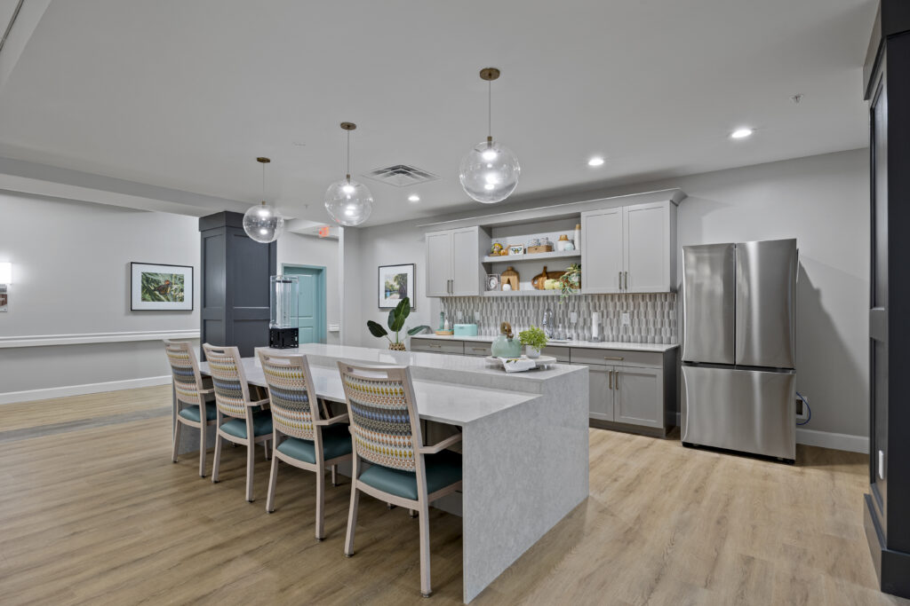Side-angle of kitchenette showcasing the counter, chairs, refrigerator, and overhead lights.