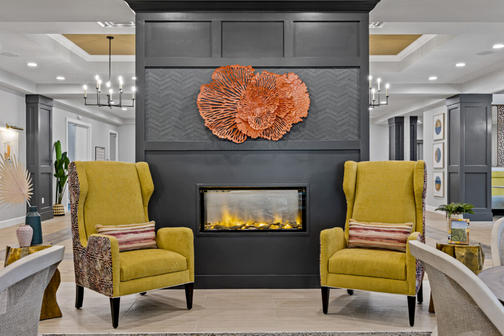 Lounge area featuring plush yellow armchairs, a modern electric fireplace, decorative wall art, and elegant chandeliers.